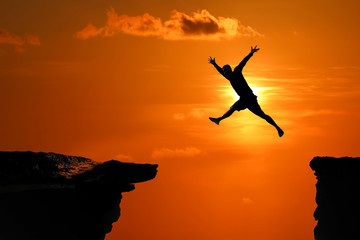 Silhouette of Men are jumped between high cliff at a red sky sunset