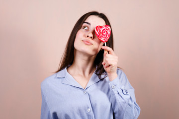 Wall Mural - Cute funny woman having fun with heart shaped lollipop, studio shoot