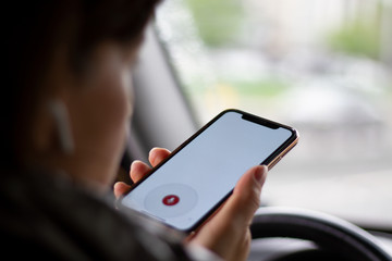 Voice Assistant helps in finding information for a woman behind the wheel. Woman using voice assistant on a smartphone looking for information while driving a car.