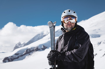 Portrait athlete skier in helmet and ski mask against the snow-capped mountains of a ski resort with a reflection of the Caucasian mountains in the mask