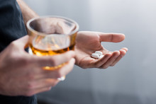 partial view of standing man holding handful of pills and glass of whiskey