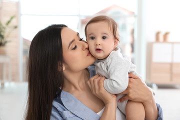 Wall Mural - Happy young mother kissing her adorable baby in living room