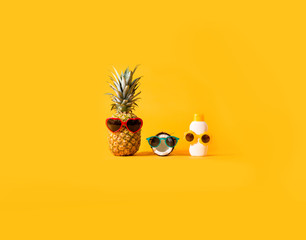 Pineapple and coconut wearing sunglasses with sunblock on a solid background