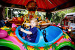 © Irina Schmidt - Adorable little toddler girl riding on funny car on roundabout carousel in amusement park. Happy healthy baby child having fun outdoors on sunny day. Family weekend or vacations
