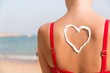 © sosiukin - Beautiful girl in red swimsuit has sunblock in shape of heart at the back at the beach