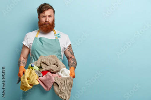Fotografía Busy dissatisfied red haired man carries basin full of laundry to washing machin