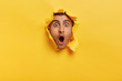 Stupefied young man with bristle keeps jaw dropped from surprisement, has popped eyes, stares through yellow torn paper, impressed by shocking rumors. People, human emotions and reaction concept