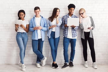 Students with various gadgets against white wall