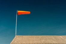Horizontally Flying Orange Windsock On Metal Rooftop And Clear Dark Blue Sky.