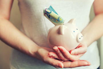 Female woman hands holding pink piggy bank and putting money Euro. Saving investment budget business wealth retirement financial money banking concept