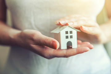 Female woman hands holding small miniature white toy house. Mortgage property insurance dream moving home and real estate concept