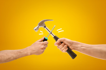 Wall Mural - Hand holding screwdriver fighting with hand holding hammer on yellow background