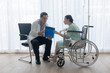 © kokotewan - The senior male doctor talked and inquired about the patient's illness at the wheelchair of the patient.