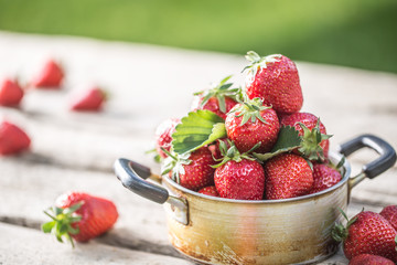 Fresh ripe strawberries in vintage kitchen pot on old garden table