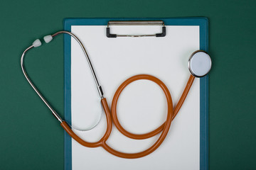 Doctor workplace - orange stethoscope and empty clipboard on green paper background