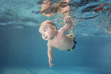 Wall Mural - Little baby boy learning to swim underwater in a swimming pool. Healthy family lifestyle and children water sports activity. Child development, disease prevention