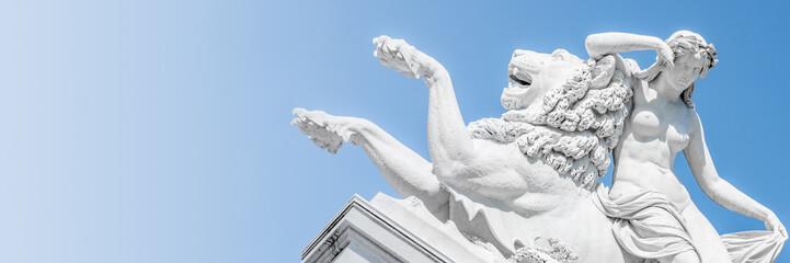 Banner of an ancient statue sensual Renaissance Era woman laying on big lion with blue sky gradient background in Potsdam, Germany, details, closeup