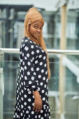 Wall Mural - Smiling young islamic African woman wearing fashionable headscarf and dress smiling cheerfully at camera whle standing in a metro train station