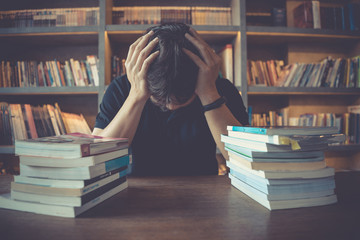 Stress and tired man under mental pressure while reading book preparing examination in library.