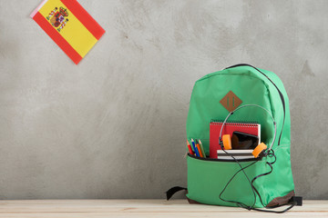 Fototapete - green backpack, flag of the Spain and school supplies, smartphone and headphones against a cement wall