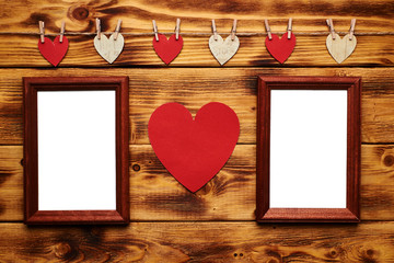 Two empty photo frames hanging on the wooden background with many hearts and garlands. Valentines day concept.