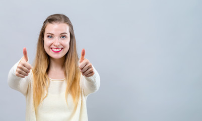 Wall Mural - Young woman giving thumbs up on a gray background