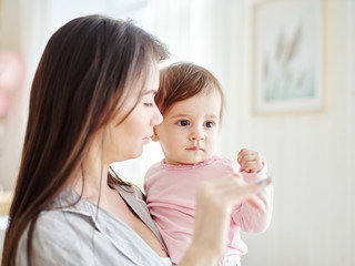 Young mother holding baby daughter in arms and teaching her how to wave goodbye