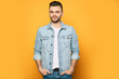 Handsome trendy and stylish beard man in denim shirt is posing over yellow background