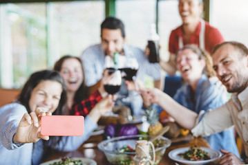 Group of happy friends taking selfie using mobile smart phone camera - Young millennial people having fun at dinner time - Friendship, food and drink, technology and youth lifestyle concept