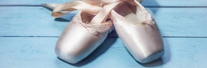 Wall Mural - Pointe shoes ballet dance shoes with a bow of ribbons beautifully folded on a wooden background.