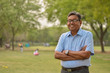 Portrait of a happy senior Indian man wearing a suit in the outside setting standing and thinking with hands crossed in a park in Delhi, India
