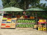 Fototapeta Kuchnia - Stargan z owocami i warzywami na sprzedaż, arbuzy, jabłka, śliwki, pomidory, ziemniaki, cytrusy, miód w słoikach i soki domowe w szkalnych butelkach