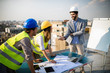 © NDABCREATIVITY - Architects team and engineers looking paper plans at construction site.