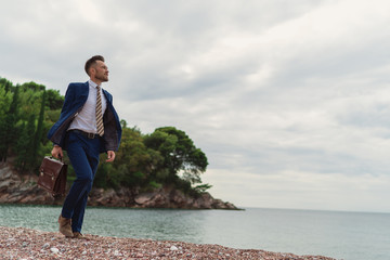 Businessman walking on the beach holding in hand briefcase