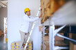 © Dusan Petkovic - Smiling young Caucasian male blue collar worker climbing ladder and checking on goods in boxed in warehouse.