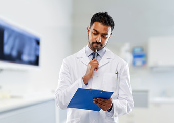 Poster - medicine, dentistry and profession concept - indian male dentist in white coat with clipboard over dental clinic office background