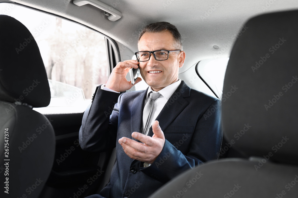 Handsome mature businessman talking by phone in car