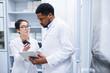 © Seventyfour - Young Asian female medical assistant in glasses showing pill bottle to black doctor and asking him about pills in storage room