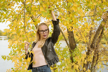 Portrait of a blonde girl with glasses on a background of yellow foliage in autumn