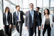 © opolja - Business People Team Walking In Modern Office, Confident Businessmen And Businesswomen In Suits Diverse With Mature Leader In Foreground.