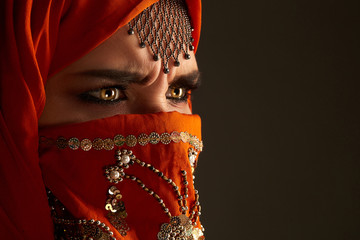 Wall Mural - Studio shot of a young charming woman wearing the terracotta hijab decorated with sequins and jewelry. Arabic style.