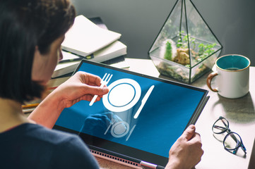 Canvas Print - Woman with laptop on her desk. She holds a restaurant icon. Concept of food order via internet. Image