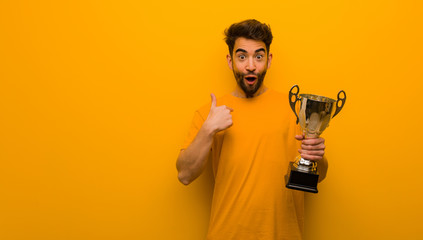 Young man holding a trophy surprised, feels successful and prosperous