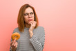 © Asier - Young woman holding a donut looking sideways with doubtful and skeptical expression.