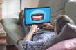 © GENETTICA - Dental insurance concept. Young man lying on the sofa watching on laptop an illustration of smiling mouth with beautiful teeth protected by a motorbike helmet. All screen graphics are made up.