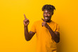 © Asier - Young black man wearing rastas over yellow background shocked pointing with index fingers to a copy space.