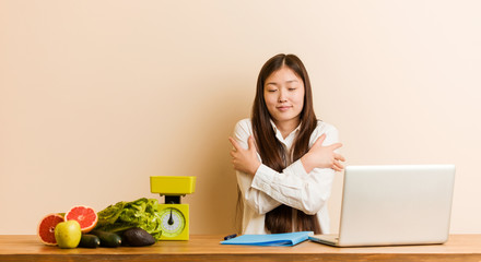 Wall Mural - Young nutritionist chinese woman working with her laptop hugs himself, smiling carefree and happy.