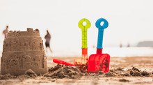 Castle Sand And Children's Toy On The Sand Beach.Plastic Bucket And Shovel Toy For Kid Play On The Sea Side. Travel On The Beach Concept