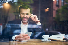 Handsome Businessman Talking On Phone In Wireless Headphones In Cafe
