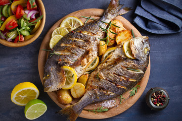 roasted fish and potatoes, served on wooden tray. overhead, horizontal - image